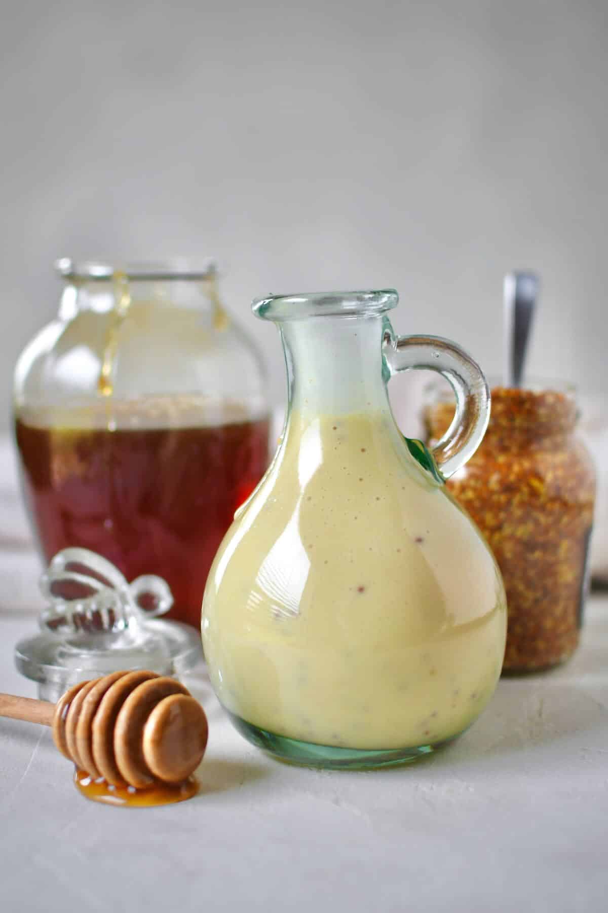 Dressing mixed up and placed in a storage bottle for later use. A honey jar and mustard jar sit behind it with a dripping honey dipper in front.