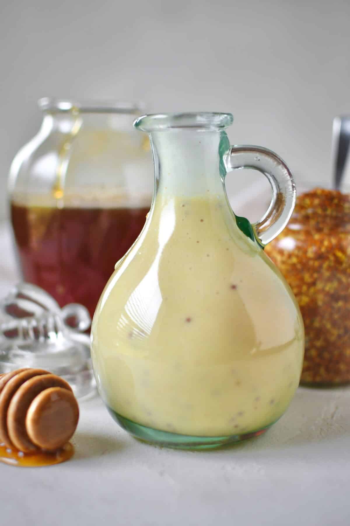 Dressing mixed up and placed in a storage bottle for later use. A honey jar and mustard jar sit behind it with a dripping honey dipper in front.