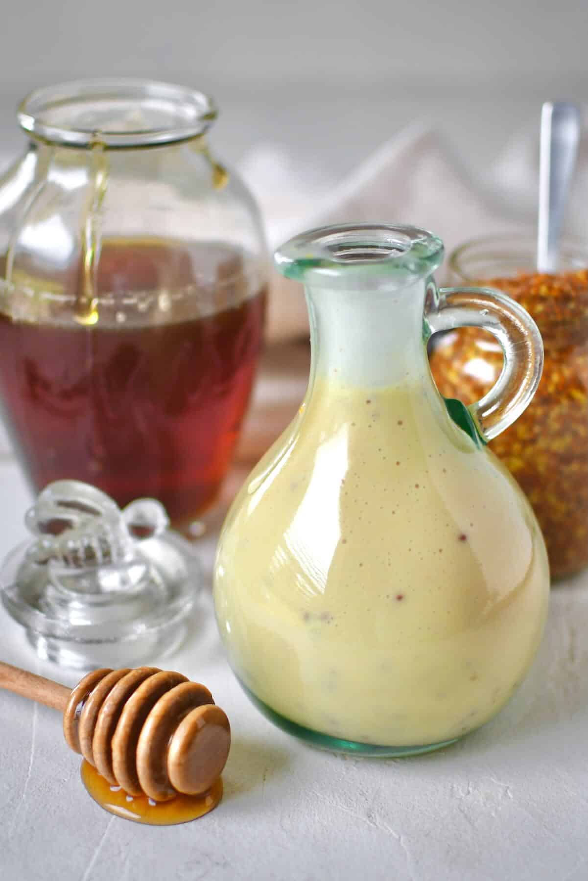 Dressing mixed up and placed in a storage bottle for later use. A honey jar and mustard jar sit behind it with a dripping honey dipper in front.