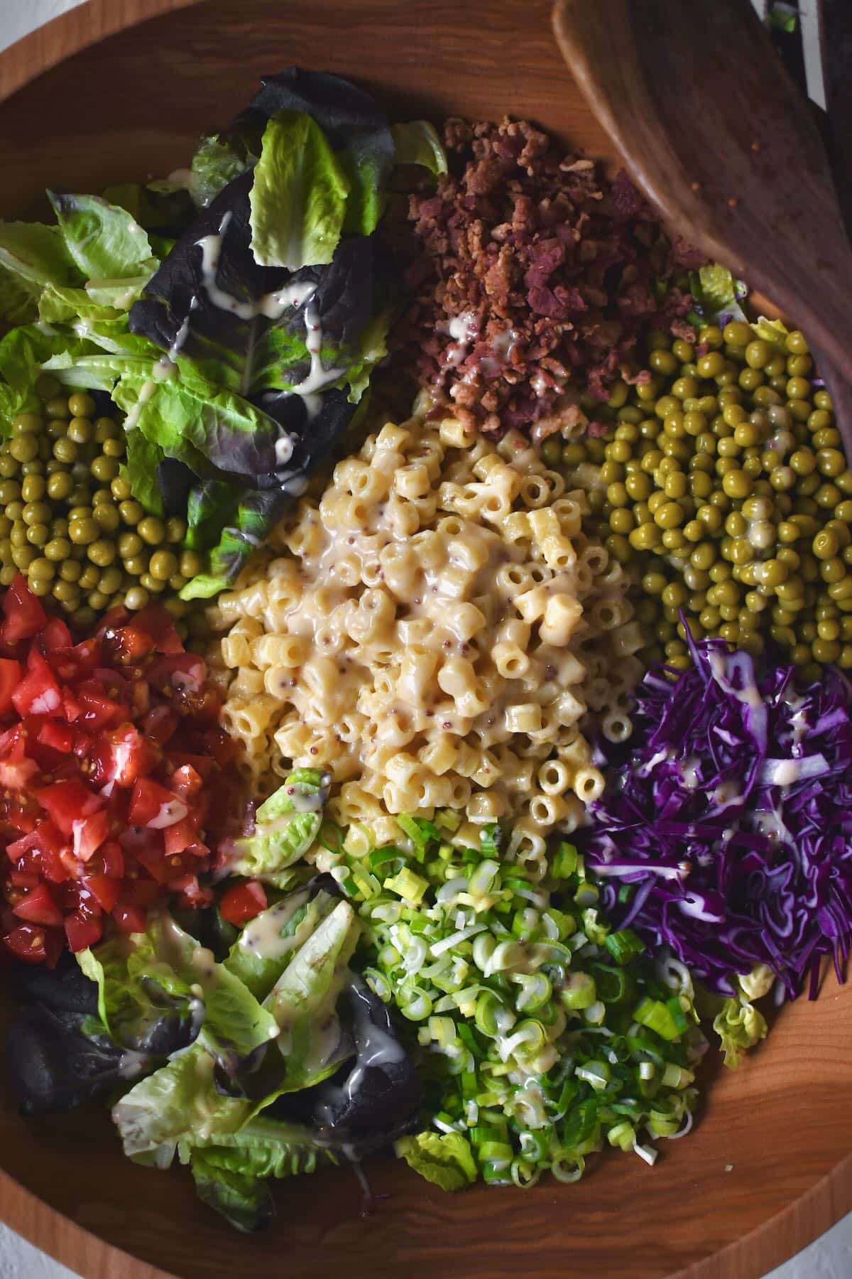 Adding all the toppings to the dressed greens before mixing it all together.