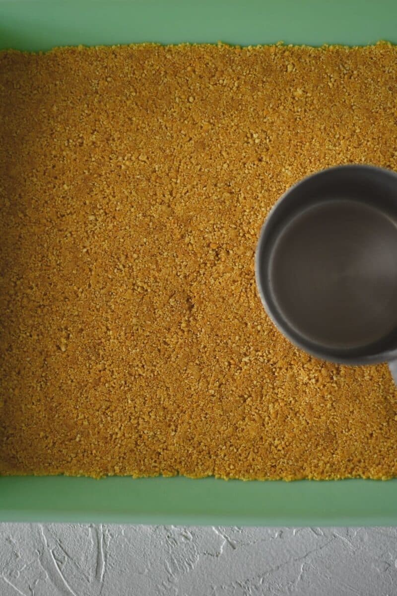 Pressing the graham cracker crust into the pan before baking.