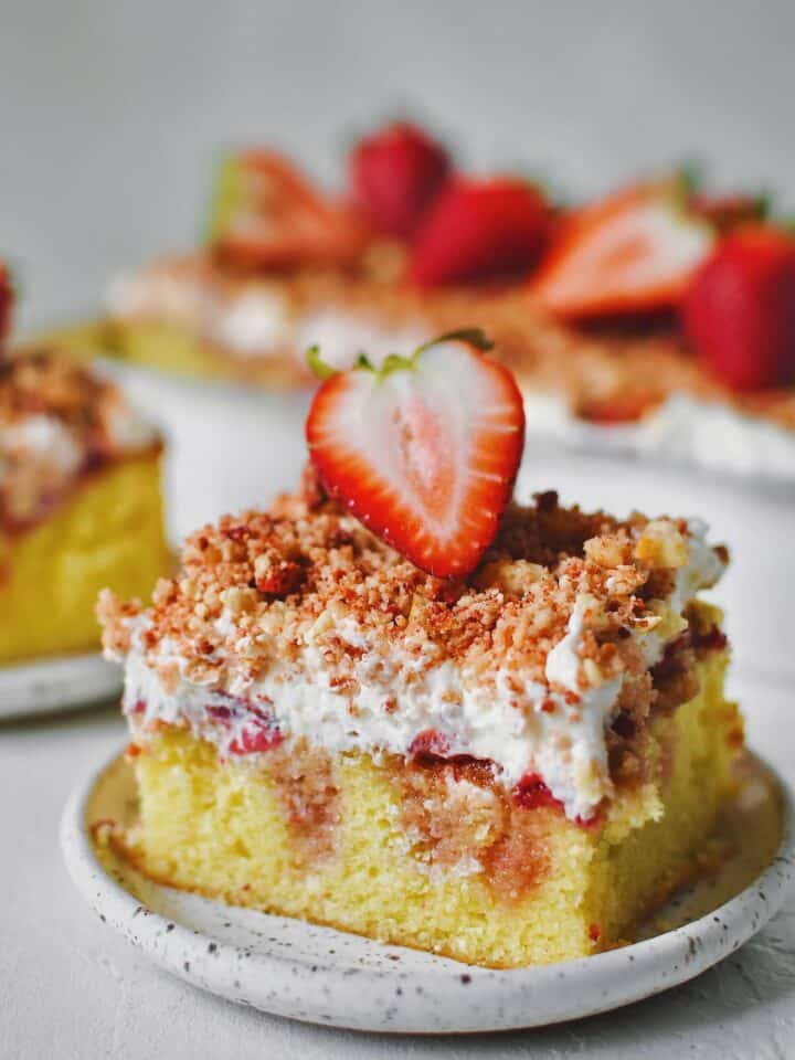 A slice of Strawberry Crunch Cake removed from the pan with a fresh strawberry on top.
