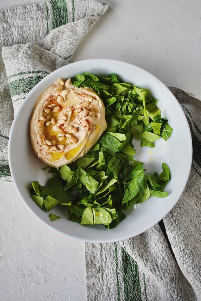 Assembling a Mediterranean Bowl, starting with spinach and hummus in the bowl.