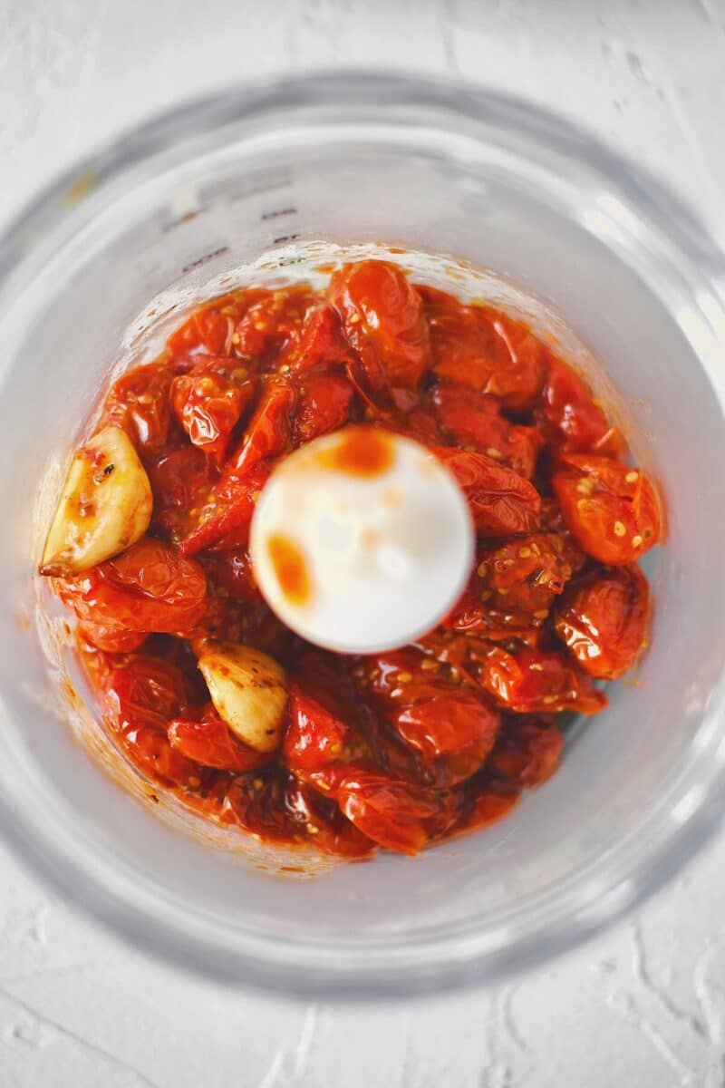 Placing the roasted tomatoes in a mini food processor so they can be blended.