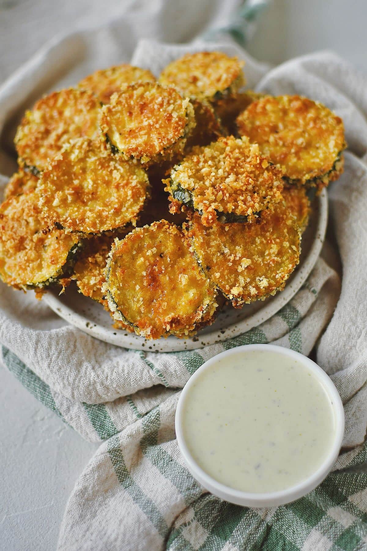 Zucchini Chips after baking, stacked on a plate and ready to eat with a side of ranch.