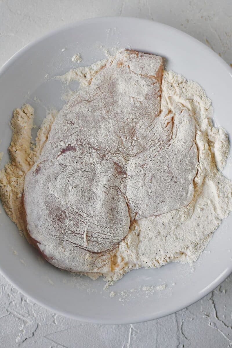 Dredging tenderized chicken through seasoned flour.