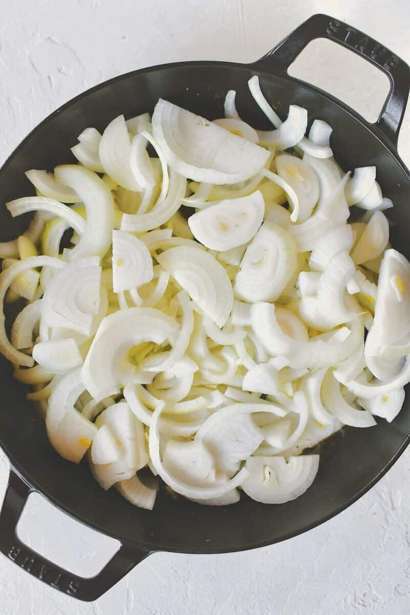 Placing the onions in the same pan after crisping the chicken thighs.