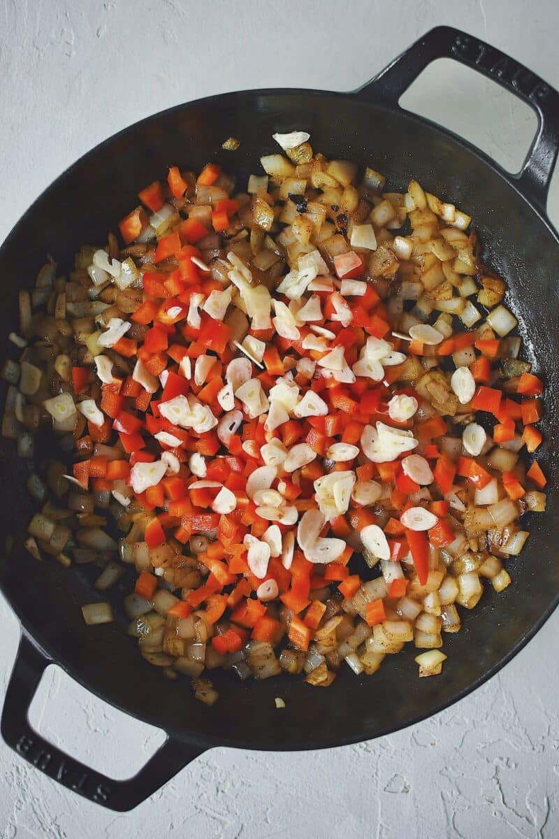 Onions sauteed until golden in bacon fat, adding the diced bell pepper and sliced garlic to the pan.