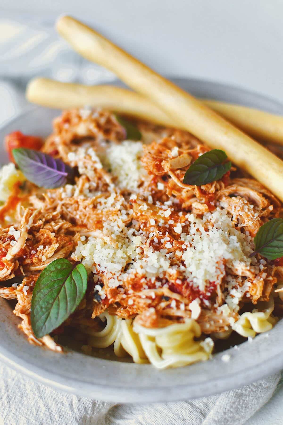 Chicken Marinara served in a bowl over pasta, topped with basil and served with grissini breadstick on the side.