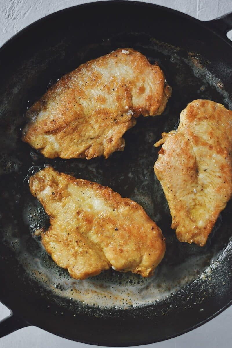 Cooking dredged chicken in a hot skillet till browned in olive oil.