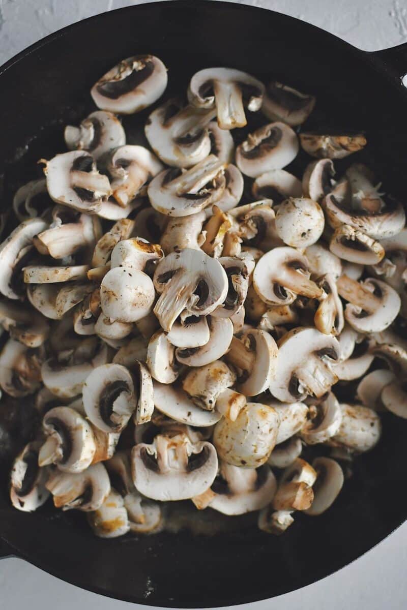 Adding the mushrooms to the pan after cooking the chicken.