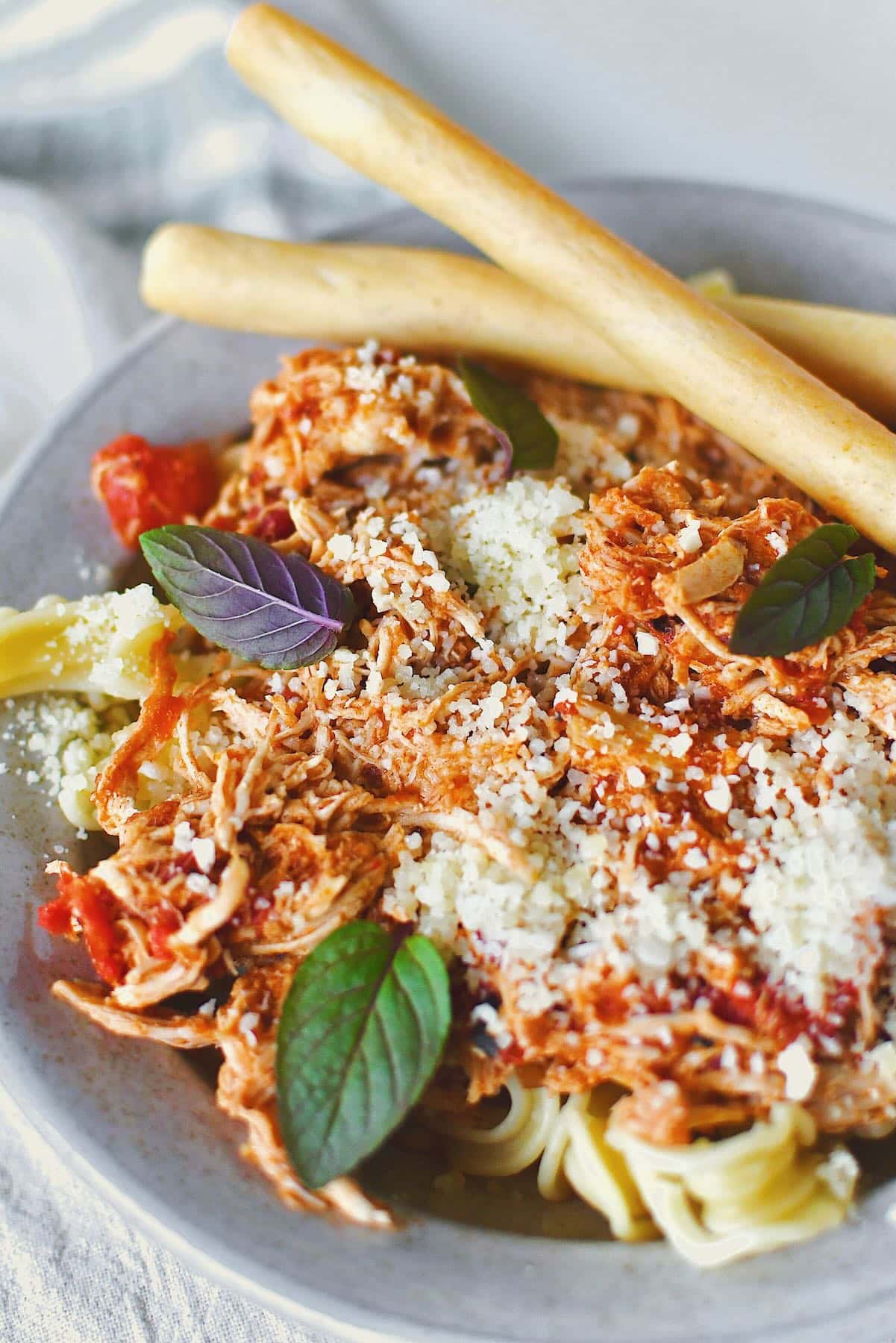 Chicken Marinara served in a bowl over pasta, topped with basil and served with grissini breadstick on the side.