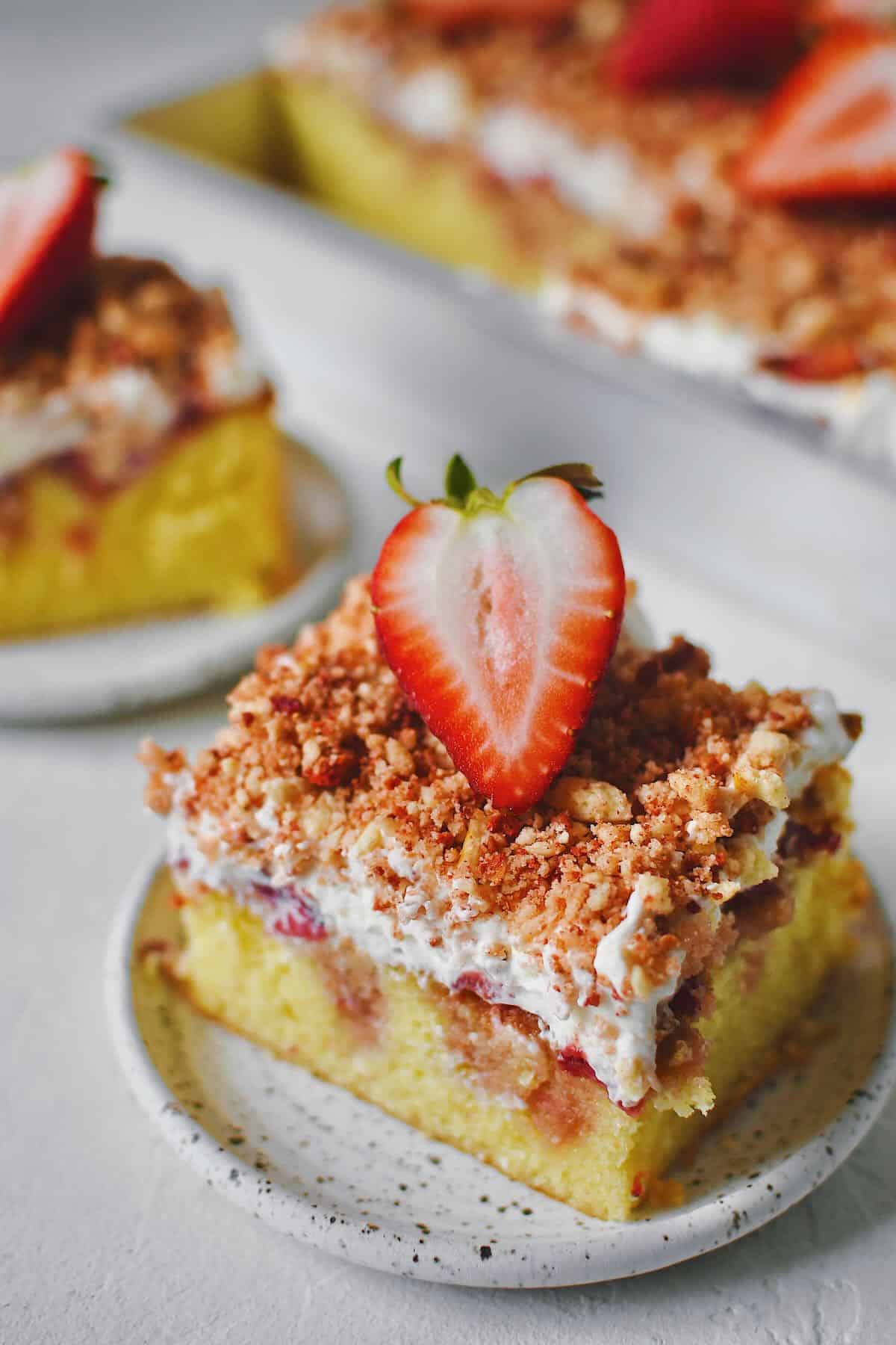 A couple slices of Strawberry Crunch Cake removed from the pan with a fresh strawberry half on top.