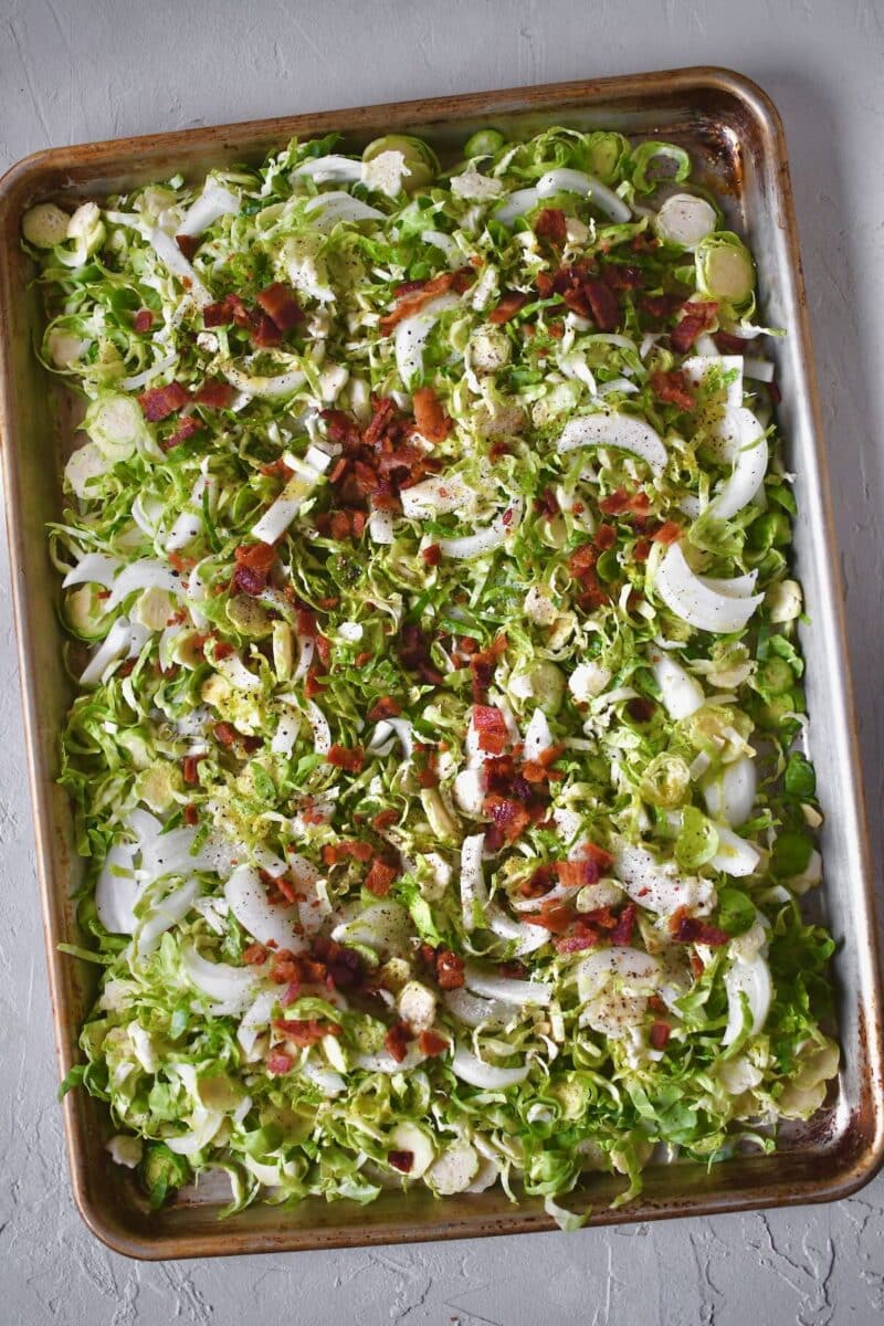 Brussel Sprouts with onion, bacon, fat, oil, and seasoning all on the pan, before tossing together.