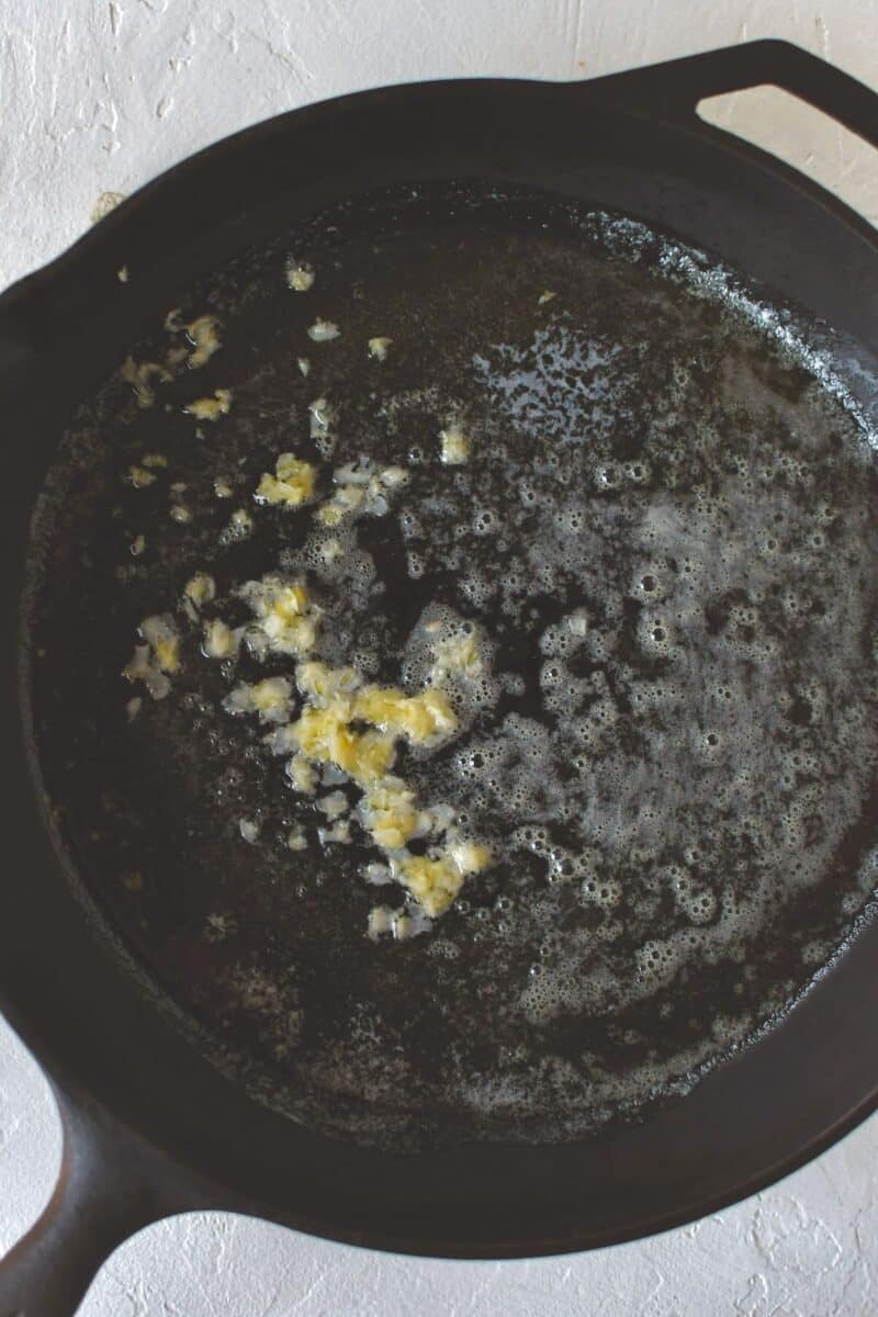 Adding the grated garlic to the melted butter in the same skillet after draining the beans.