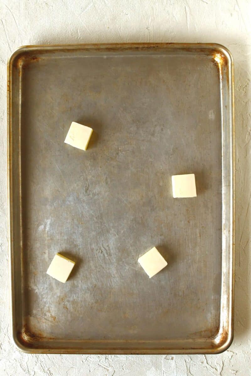 Solid butter placed on a rimmed baking sheet before melting.