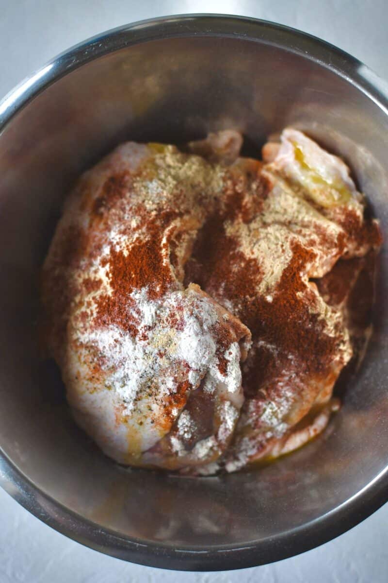 Chicken thighs in a bowl with the seasonings tossed over them.