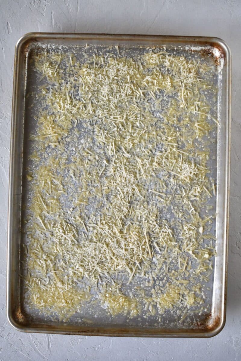 Parmesan cheese dusted over a sheet pan that has melted butter on it.