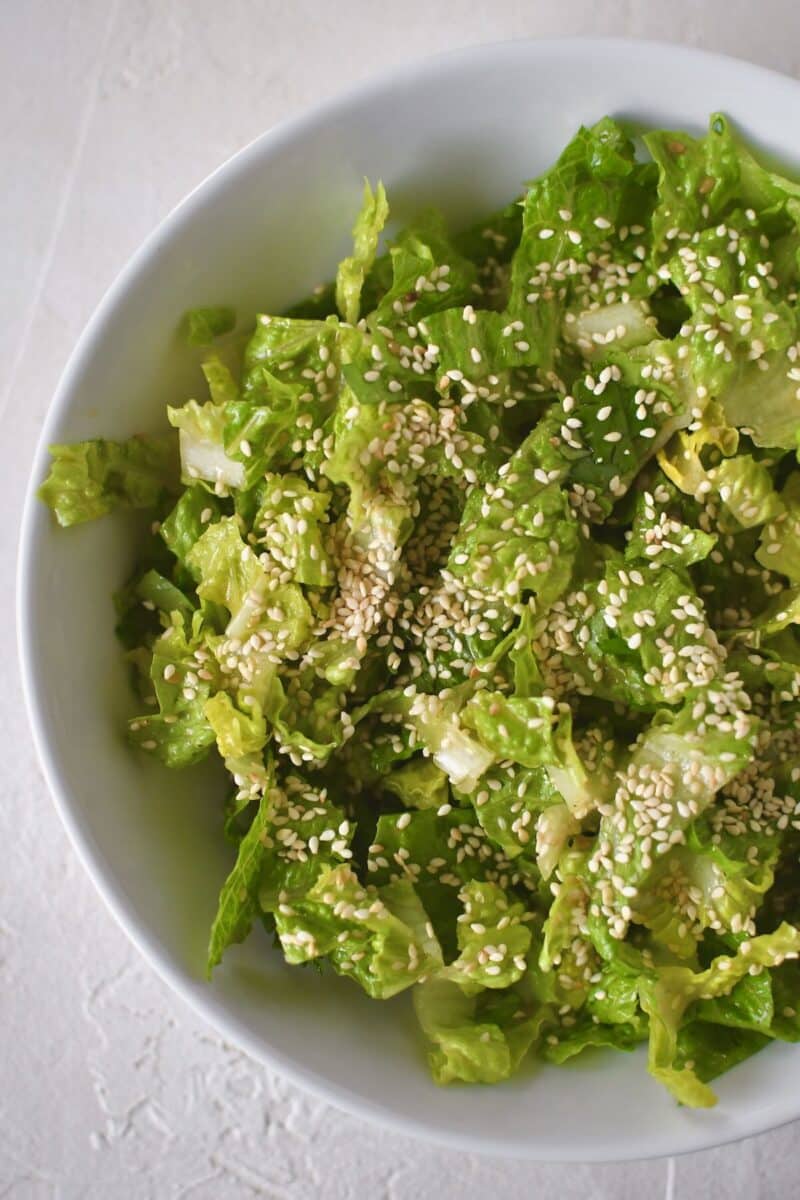 Greens that have been tossed with dressing, now placed in a serving bowl and topped with some sesame seeds.