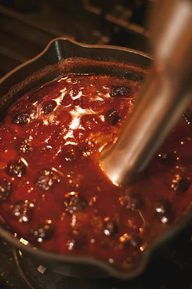 Using an immersion blender to puree the cherries, peppers, and onion to make a smooth sauce.