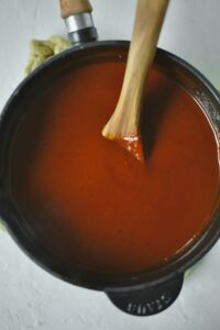 Finishes sauce in the saucepan with a spoon in it to stir.