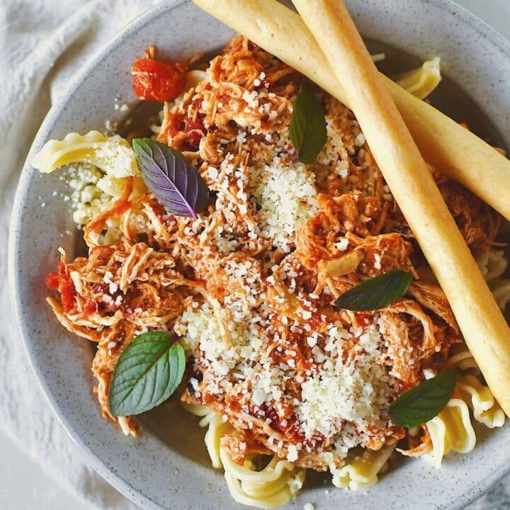 Chicken Marinara served in a bowl over pasta, topped with basil and served with grissini breadstick on the side.