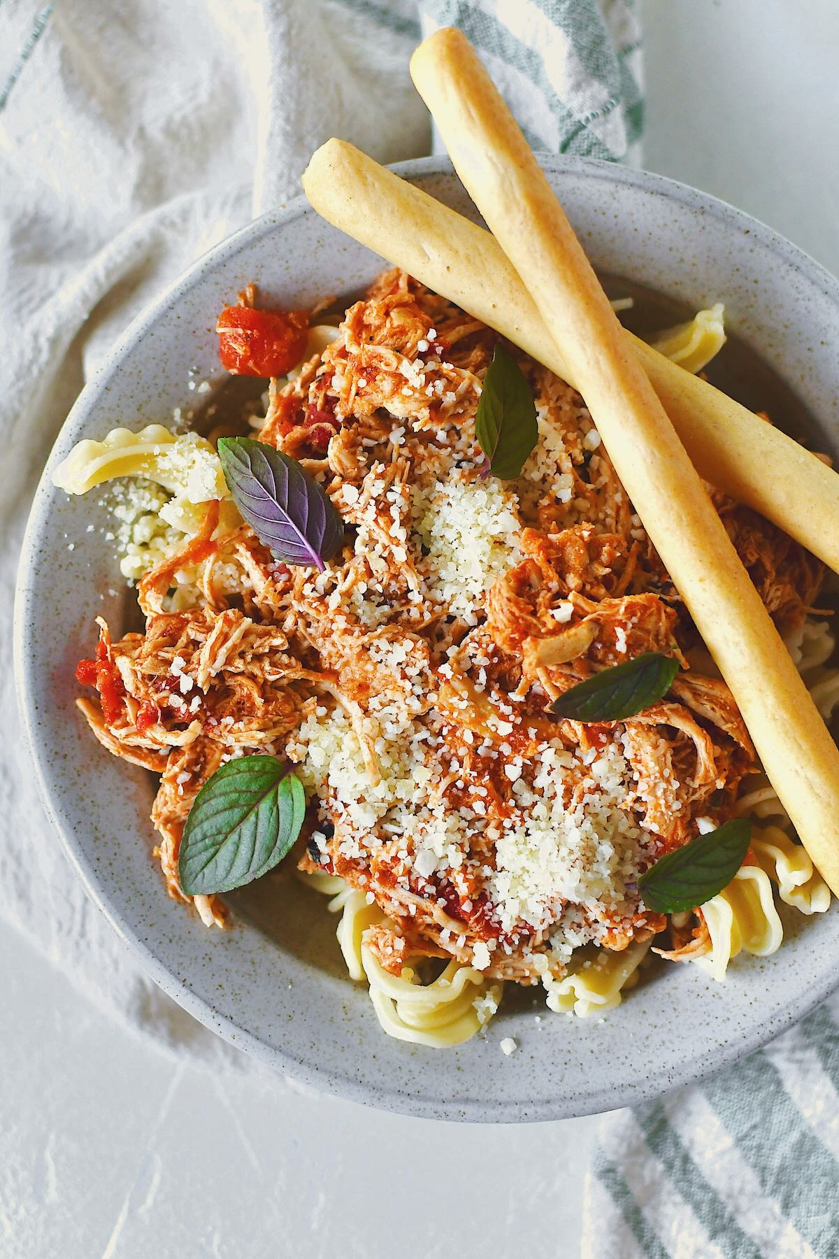 Chicken Marinara served in a bowl over pasta, topped with basil and served with grissini breadstick on the side.