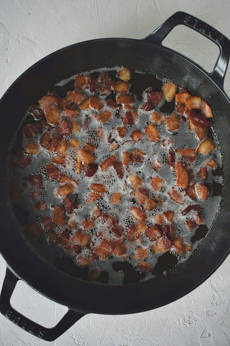 Diced bacon crisping in a large skillet.