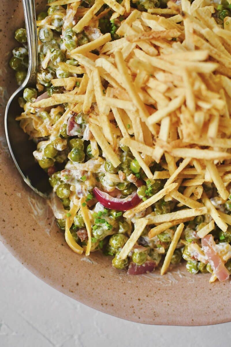 Bacon Pea Salad tossed together in a bowl and topped with shoestring potatoes.