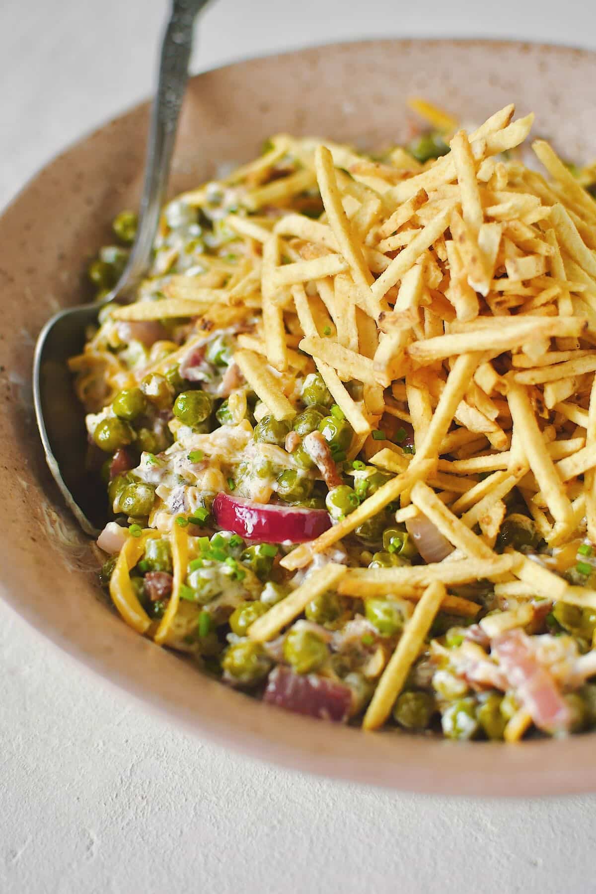 Bacon Pea Salad tossed together in a bowl and topped with shoestring potatoes.