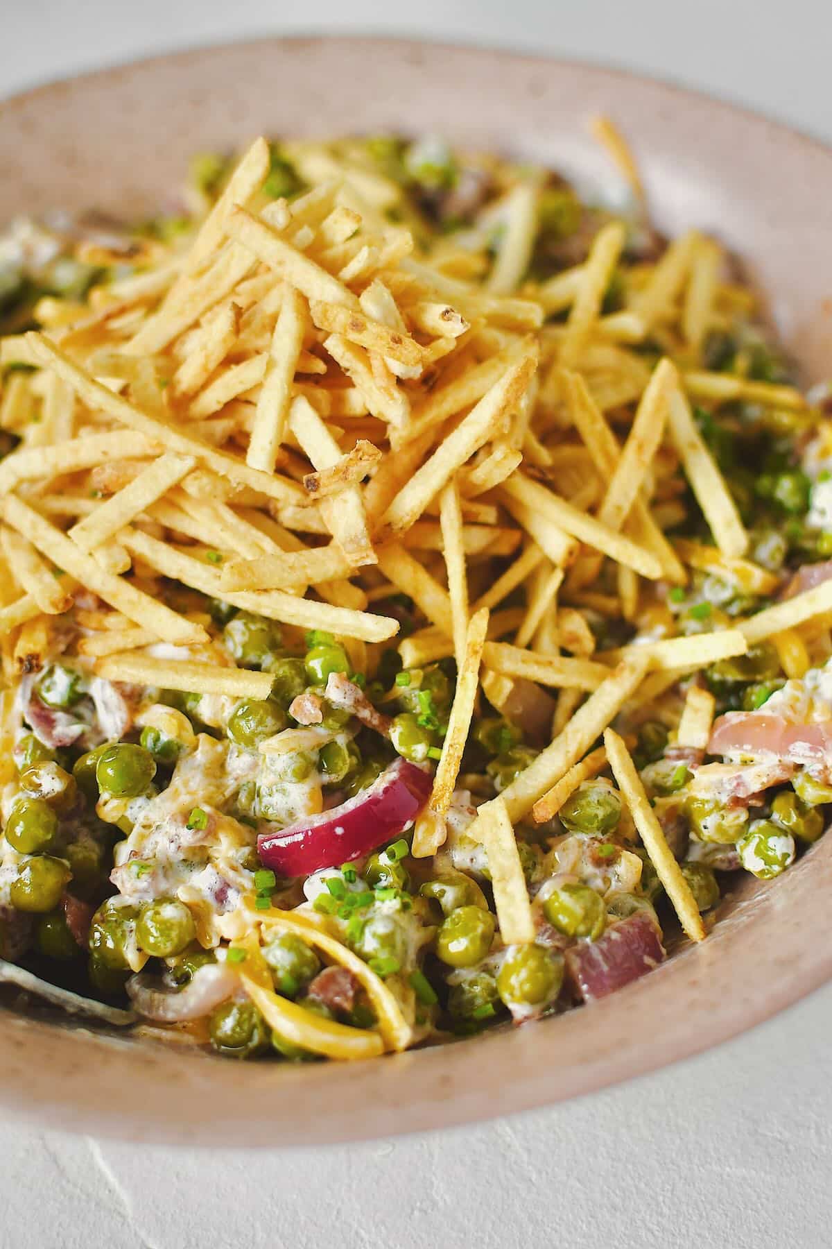 Bacon Pea Salad tossed together in a bowl and topped with shoestring potatoes.