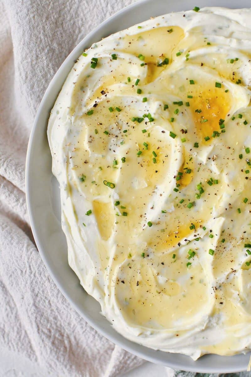 Whipped Goat Cheese spread on a plate and topped with lavender honey, chives, and sea salt.