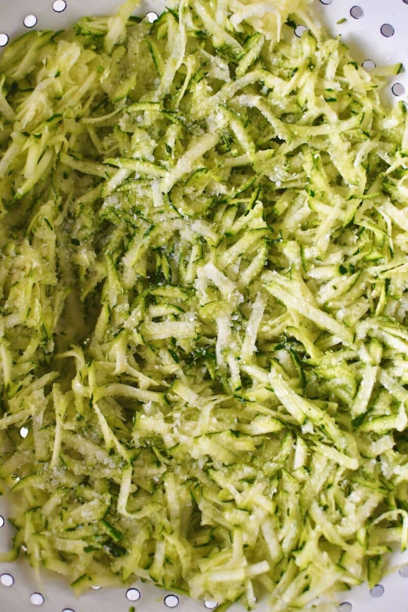 Shredded zucchini in a colander, that has been tossed with salt and left to rest for a few minutes.