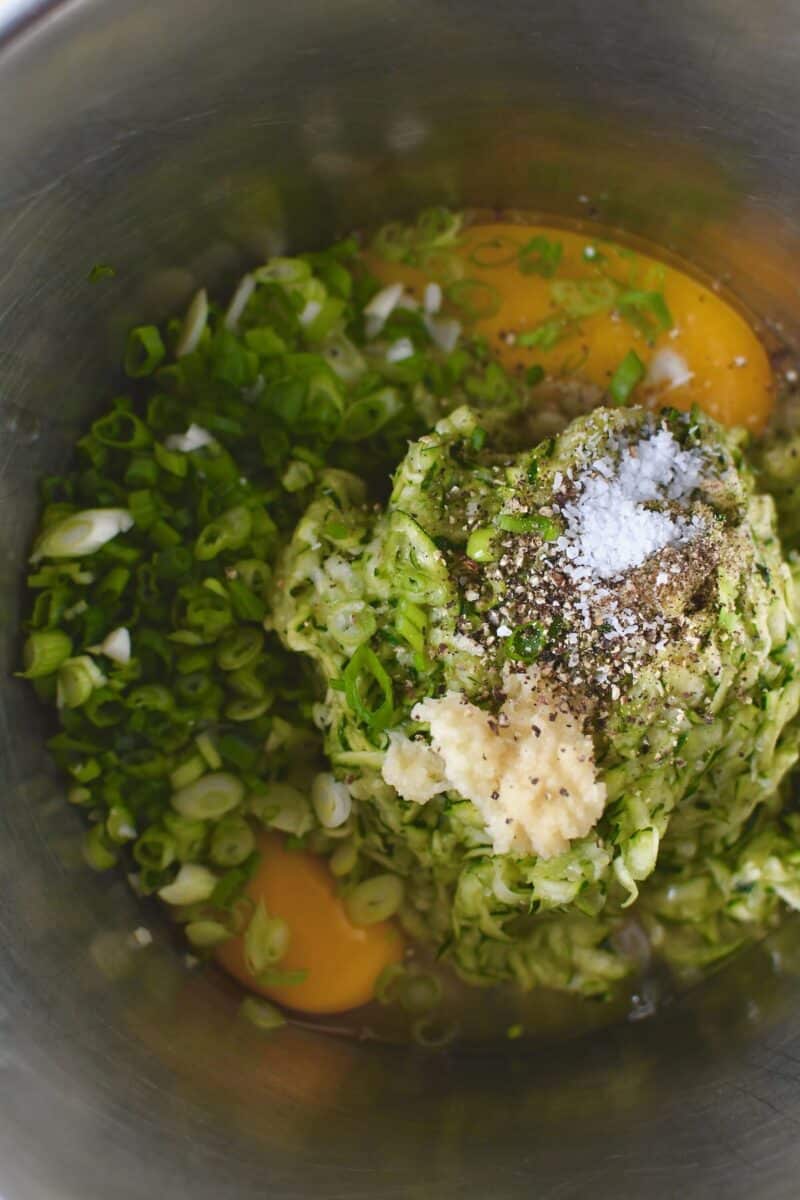 Adding the squeezed zucchini to a bowl with the egg, salt, pepper, garlic, and green onions.