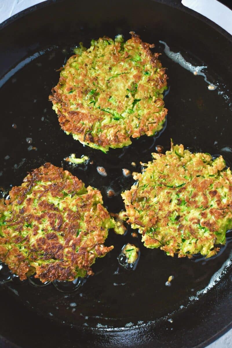 Golden zucchini fritters after flipping, cooking the second side till golden.