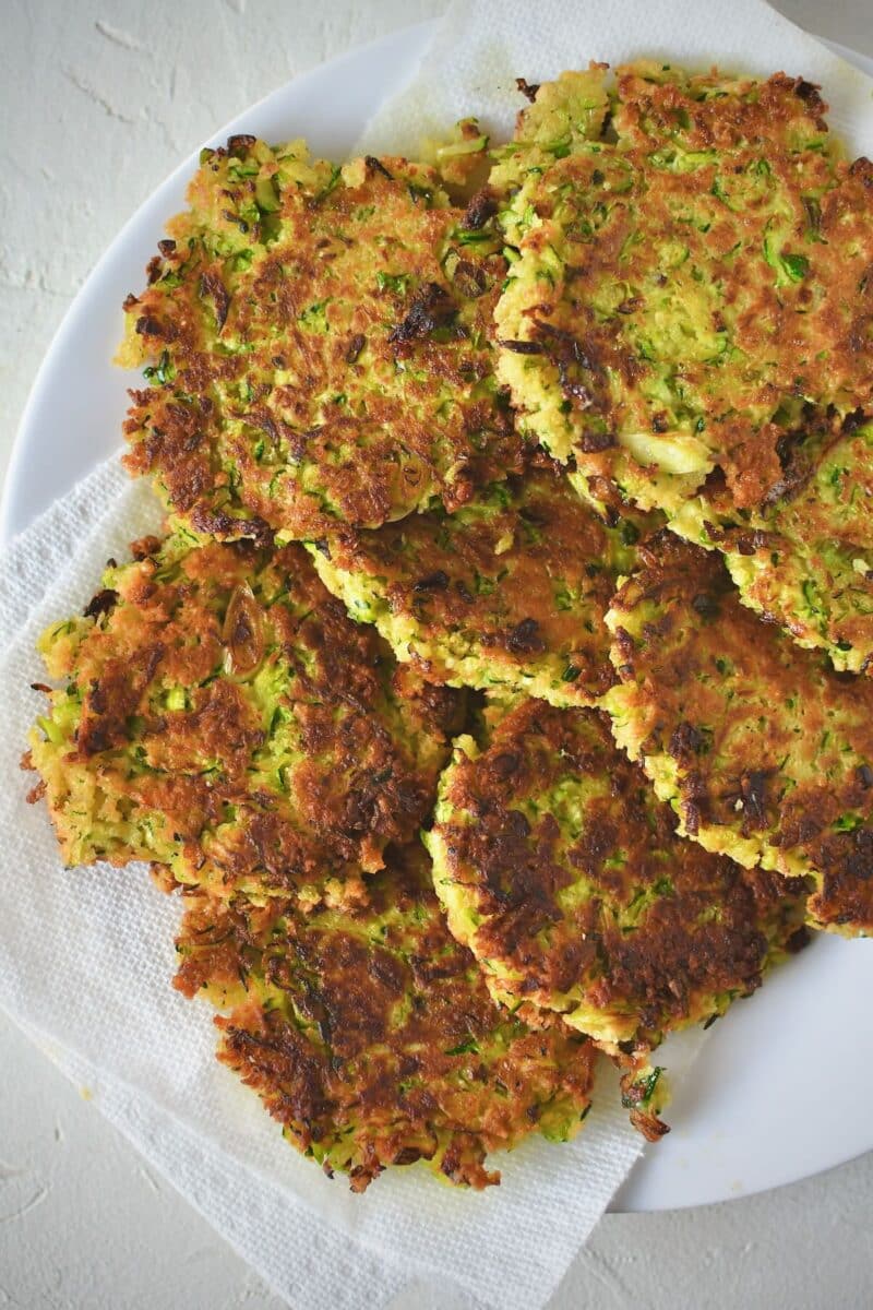 Zucchini fritters after frying, resting on a paper towel lined plate.
