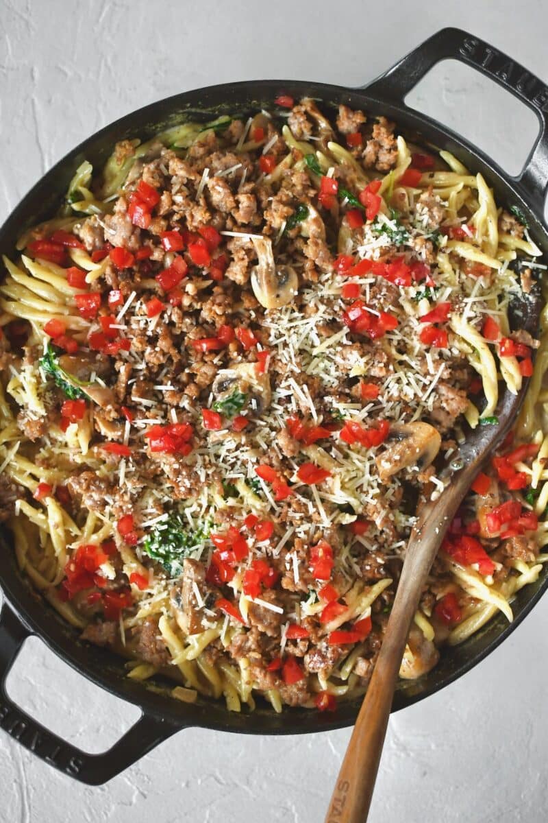 Returning the sausage to the pan and topping with tomatoes and parmesan.