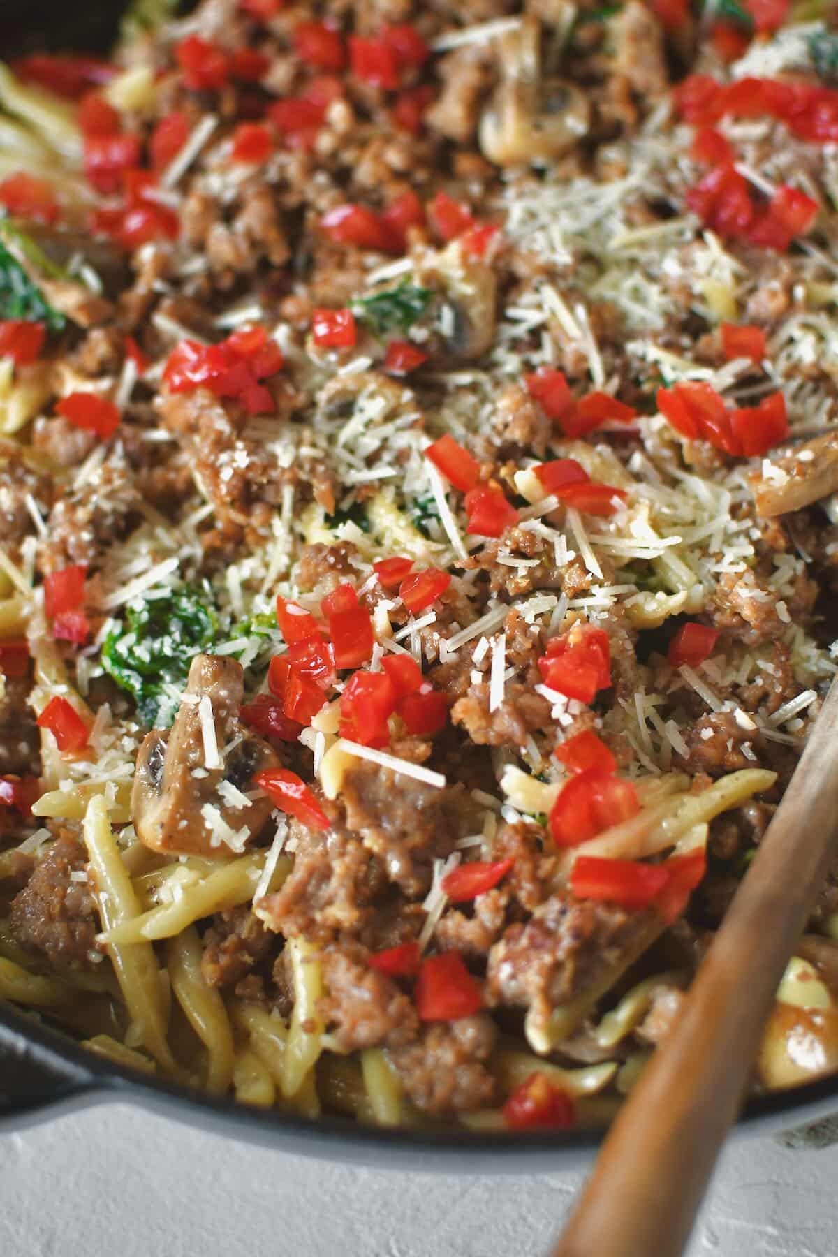 Returning the sausage to the pan and topping with tomatoes and parmesan.