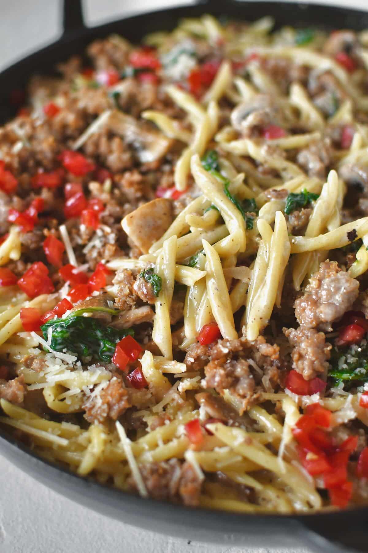 Returning the sausage to the pan and topping with tomatoes and parmesan.