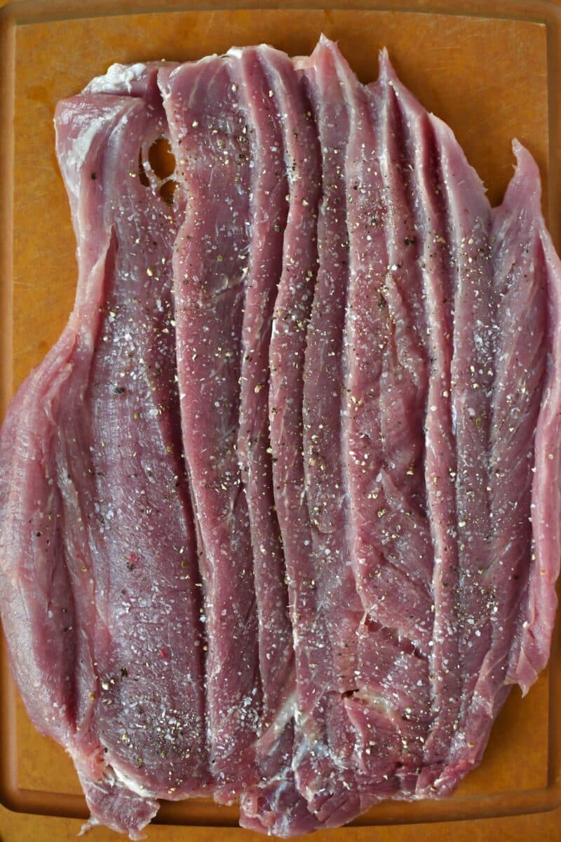 One butterflied pork tenderloin that has been seasoned with salt and pepper resting on a cutting board.