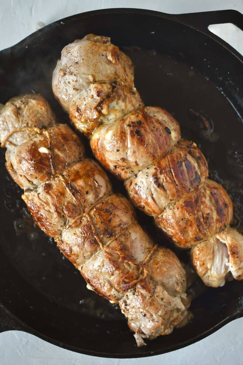 Searing the rolled and trussed pork tenderloins in a hot pan on the stove.