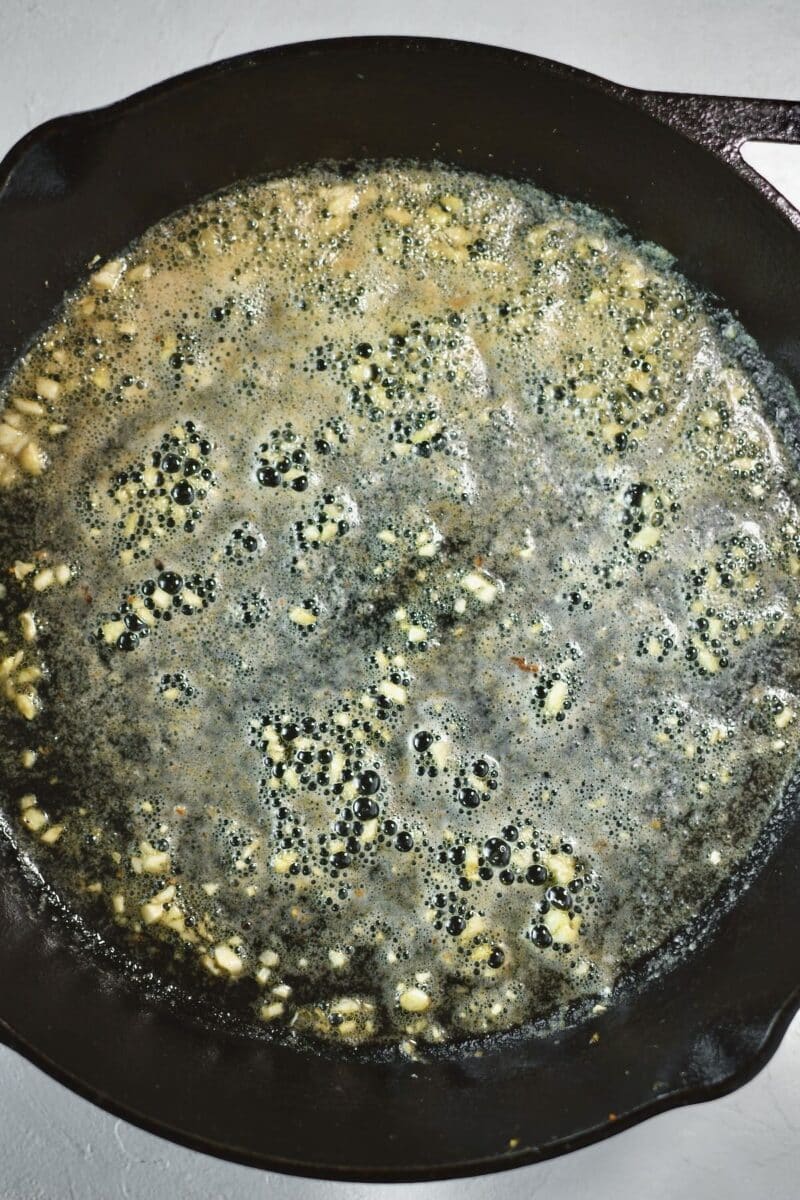 Garlic cooking in butter in a large cast iron skillet on the stove.