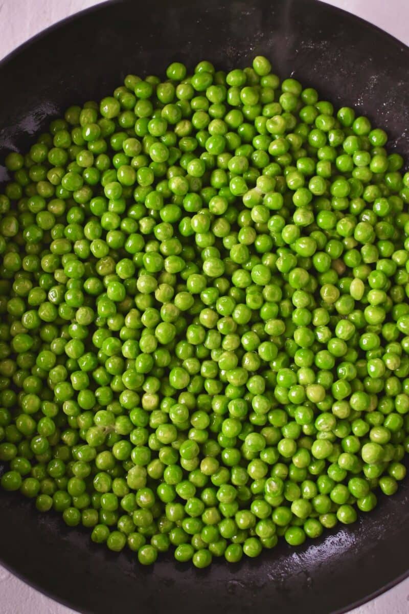 Peas warming in a pan with some butter on the stove.