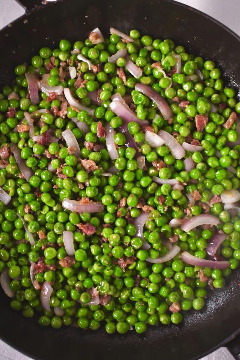 Peas cooking with red onion and bacon bits added to them.