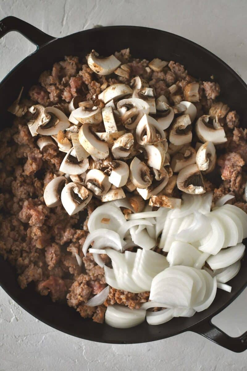 Adding diced button mushrooms and sliced onions to browning italian sausage.