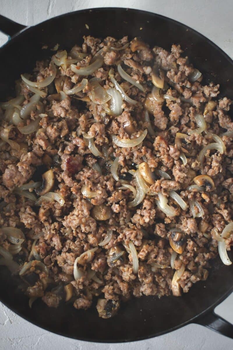 Button mushrooms and onions browned with italian sausage in a large skillet.