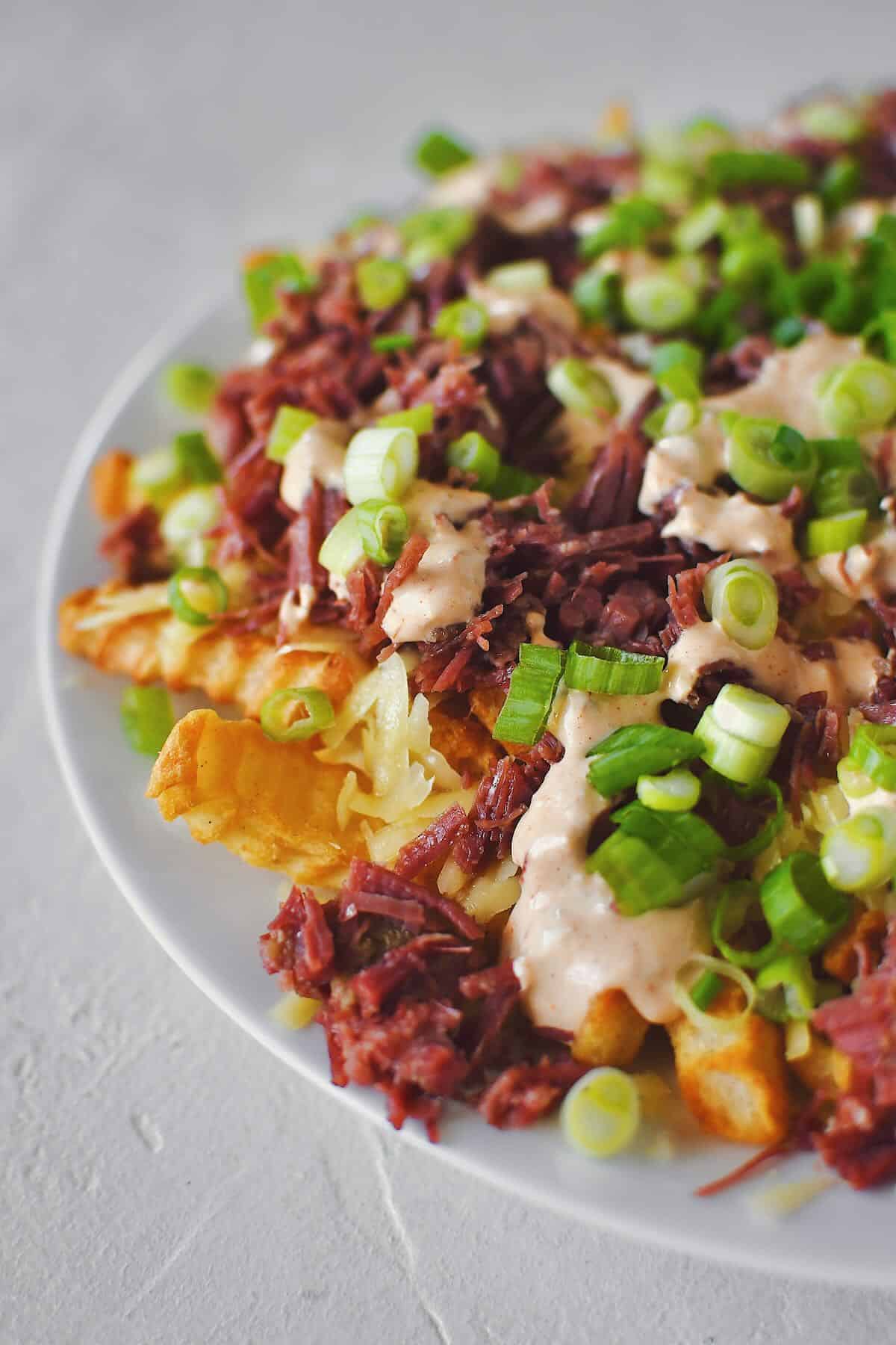 Finished Irish Nachos with white cheddar, corned beef, remoulade, and green onions on top of crispy crinkle french fries.