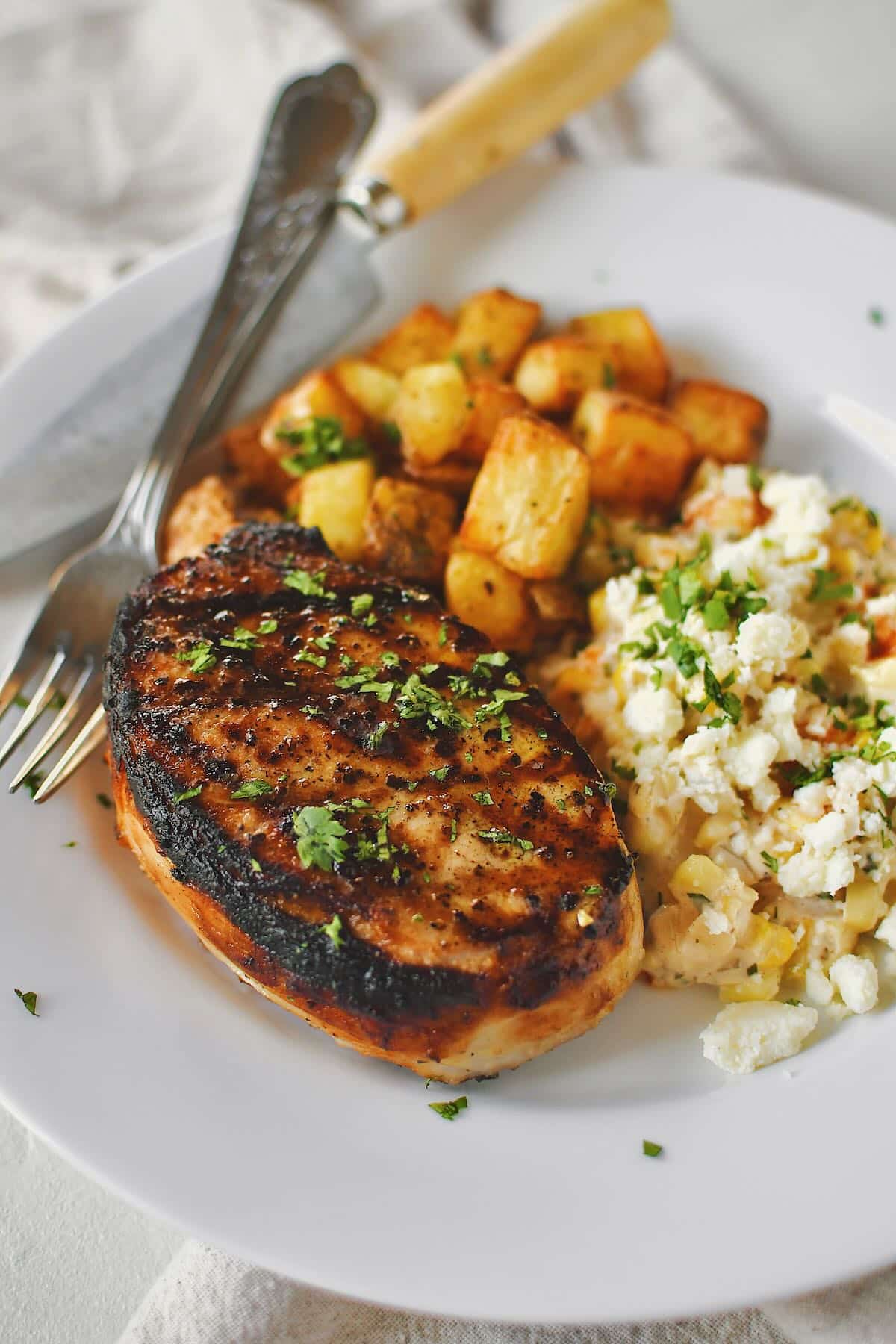 Brined Pork Chops just off the grill, ready to eat. Served with roasted potatoes and corn.