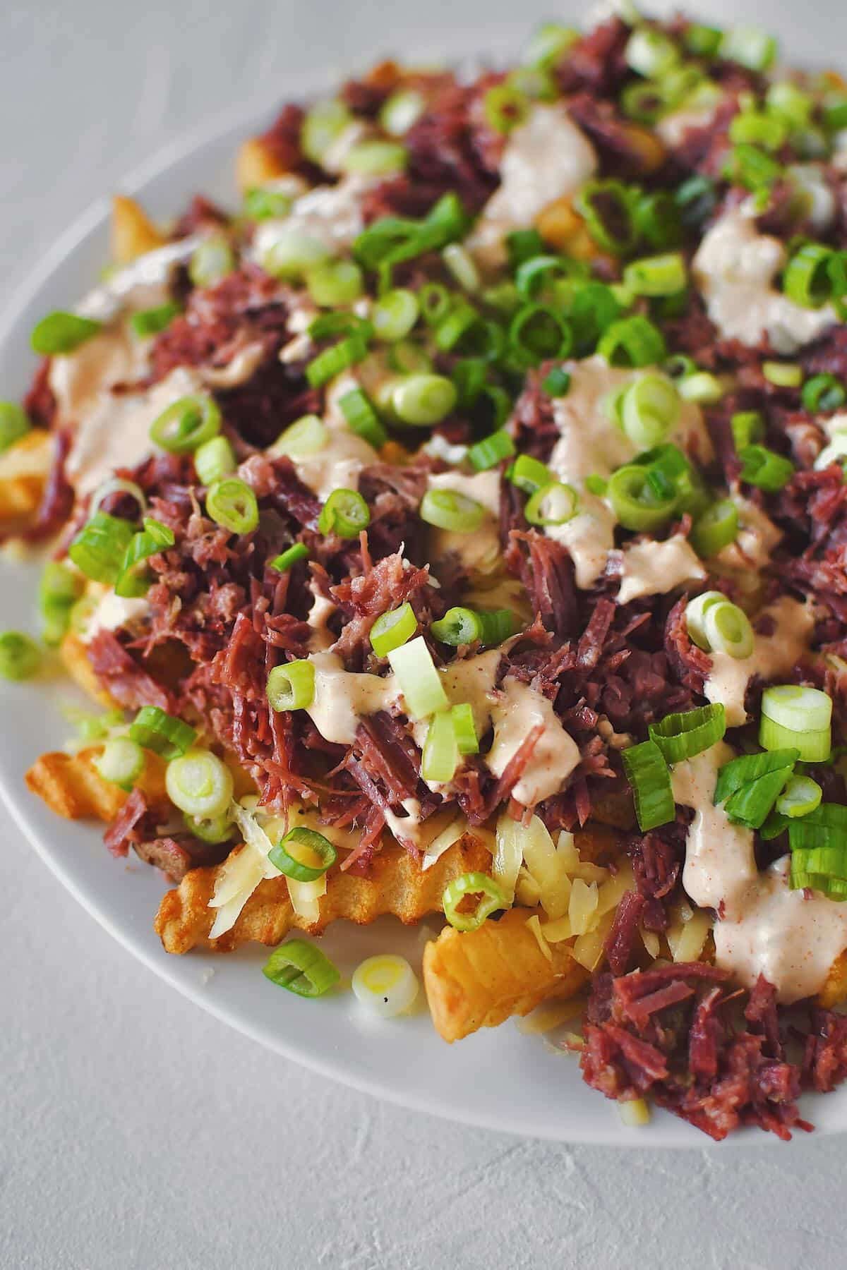 Finished Irish Nachos with white cheddar, corned beef, remoulade, and green onions on top of crispy crinkle french fries.