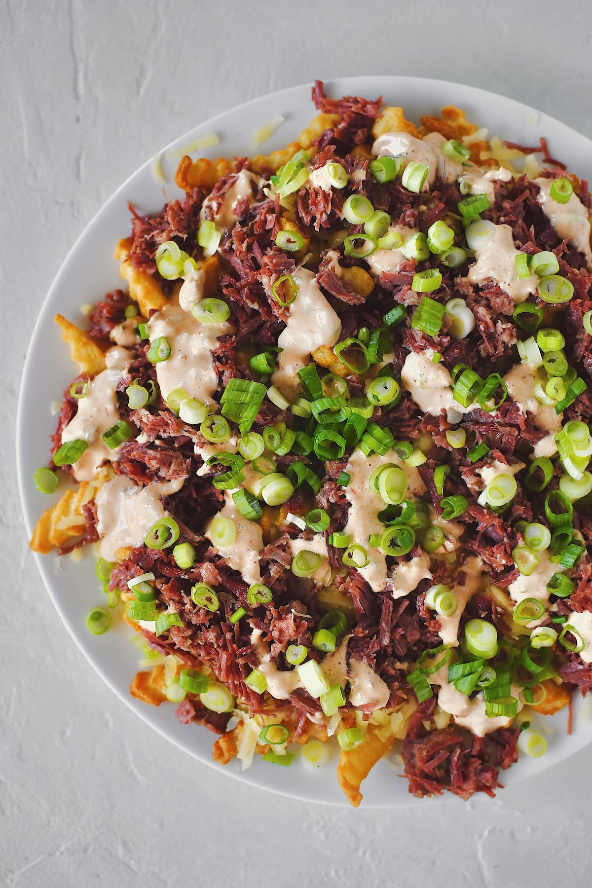 Finished Irish Nachos with white cheddar, corned beef, remoulade, and green onions on top of crispy crinkle french fries.